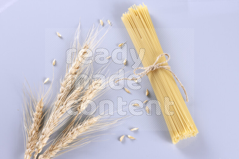Raw pasta with wheat stalks on light blue background