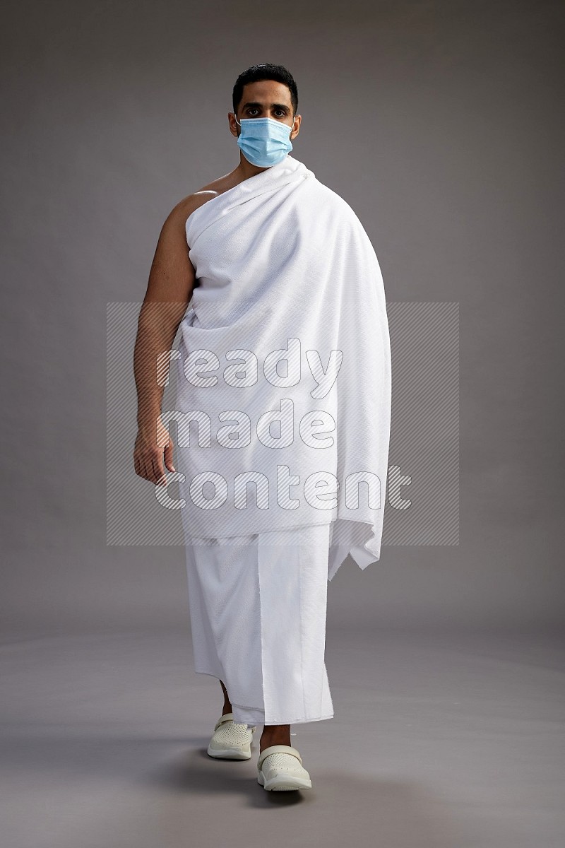 A man wearing Ehram with face mask Standing Interacting with the camera on gray background