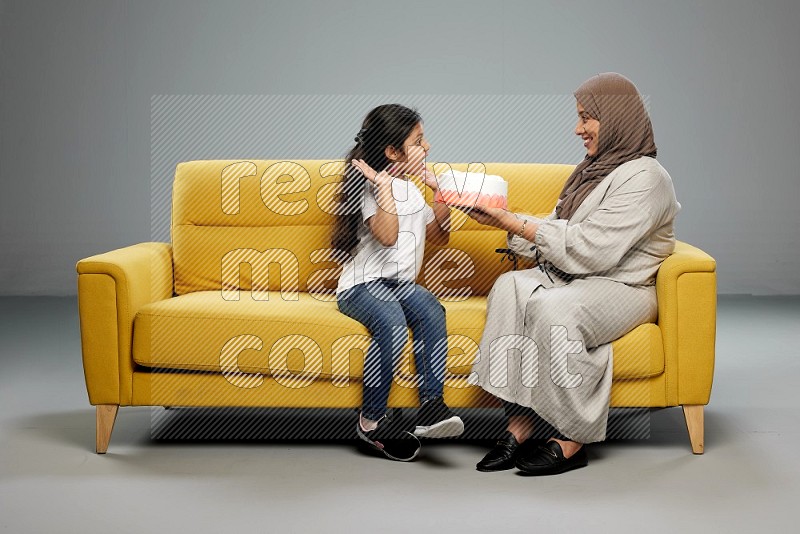 A girl sitting giving a cake to her mother on gray background