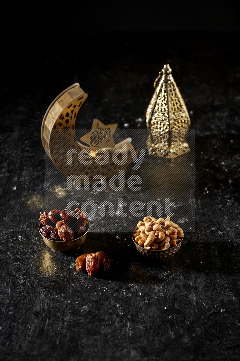 Dates in a metal bowl with cashews beside golden lanterns in a dark setup