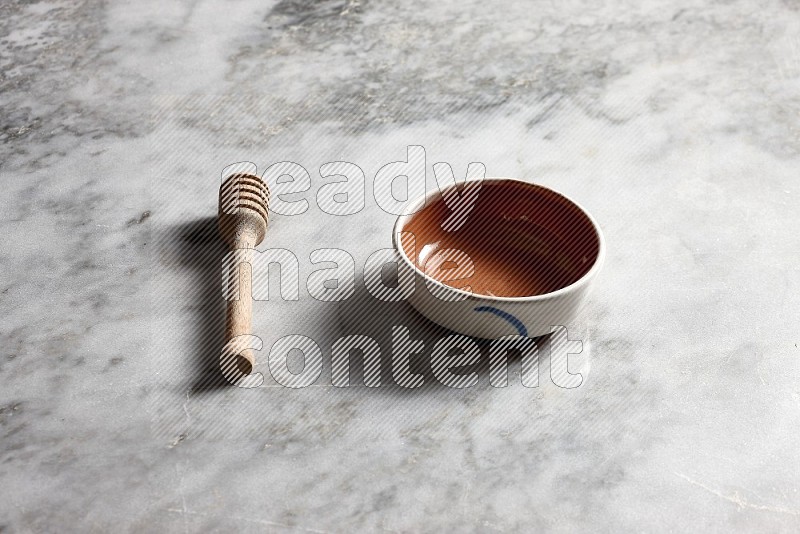 Multicolored Pottery bowl with wooden honey handle on the side with grey marble flooring, 45 degree angle