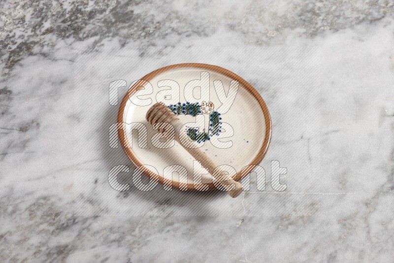 Decorative pottery plate with wooden honey dipper in it on grey marble background