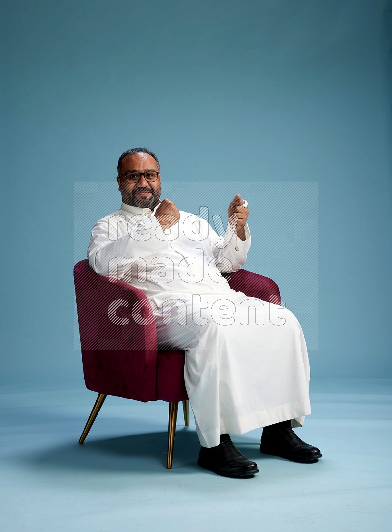 Saudi Man without shimag sitting on chair Interacting with the camera on blue background