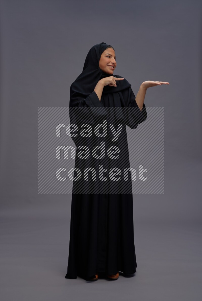 Saudi woman wearing Abaya standing interacting with the camera on gray background