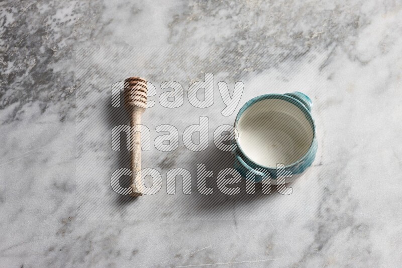 Multicolored pottery bowl with wooden honey dipper on the side on grey marble background