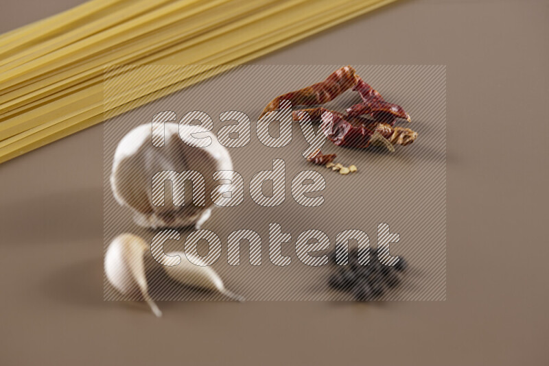 Raw pasta with different ingredients such as cherry tomatoes, garlic, onions, red chilis, black pepper, white pepper, bay laurel leaves, rosemary and cardamom on beige background