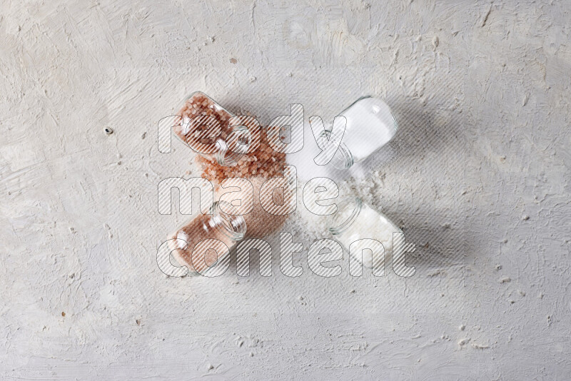 4 glass jars filled with table salt, coarse sea salt, fine himalayan salt and coarse himalayan salt on white background