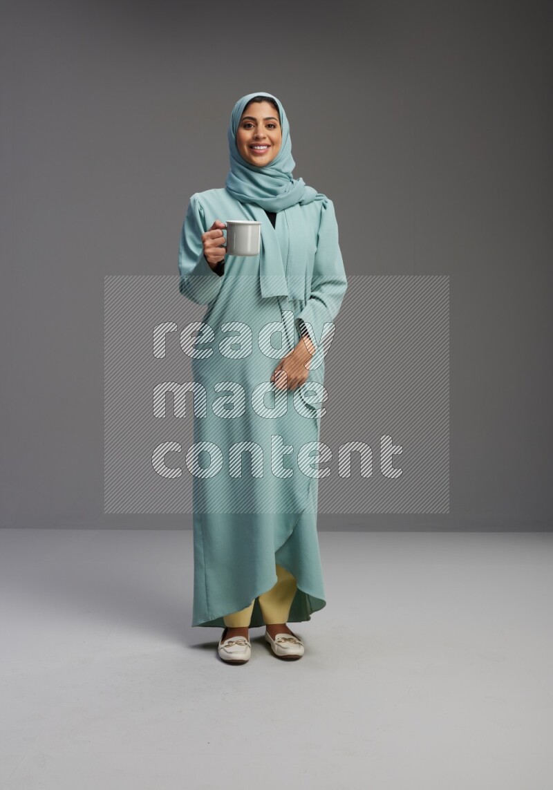 Saudi Woman wearing Abaya standing  holding a mug on Gray background