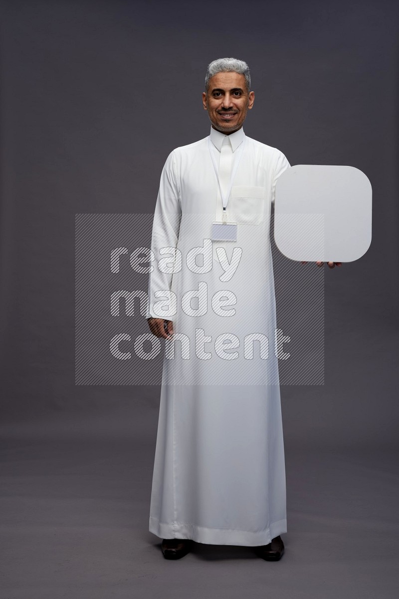 Saudi man wearing thob with neck strap employee badge standing holding social media sign on gray background