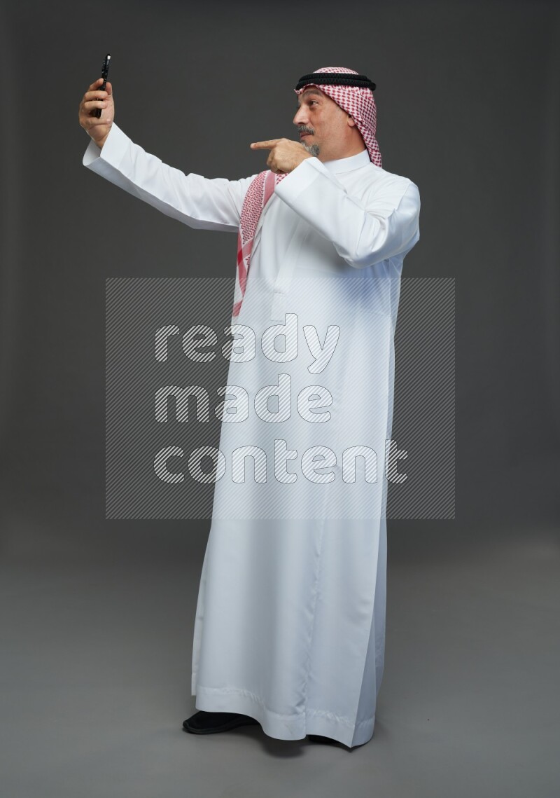 Saudi man with shomag Standing taking selfie on gray background