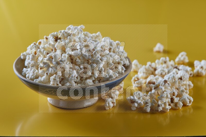 A multicolored ceramic plate full of popcorn with popcorn beside it on a yellow background in different angles