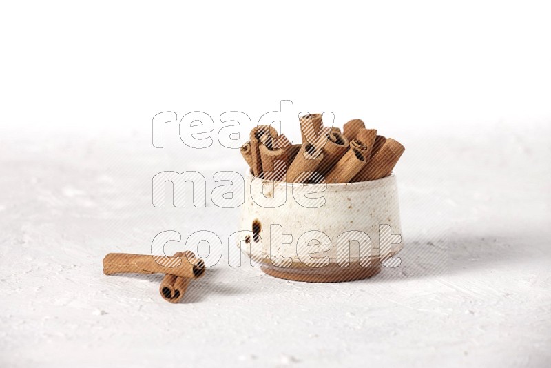 Cinnamon sticks in a beige bowl on a white background