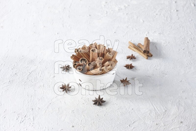 White bowl full of cinnamon sticks surrounded by star anis on a textured white background in different angles