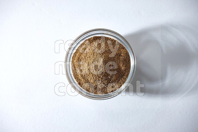A glass bowl full of cumin powder on a white flooring