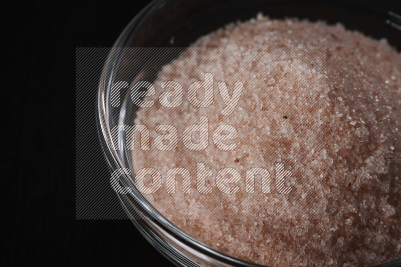 A glass bowl full of fine himalayan salt on black background