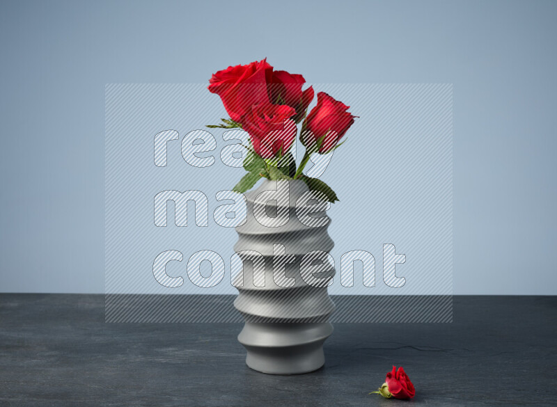 An arrangement of vivid red roses in a grey spiral vase on black marble background