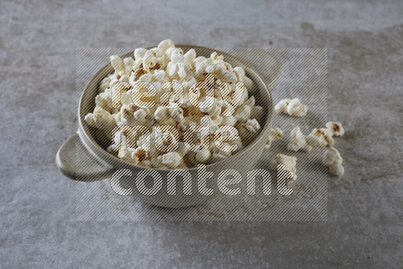 popcorn in a off-white handheld ceramic bowl on a grey textured countertop