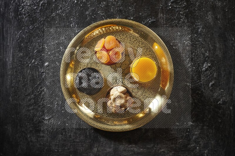 Dried fruits in metal bowls with qamar eldin on a tray in dark setup
