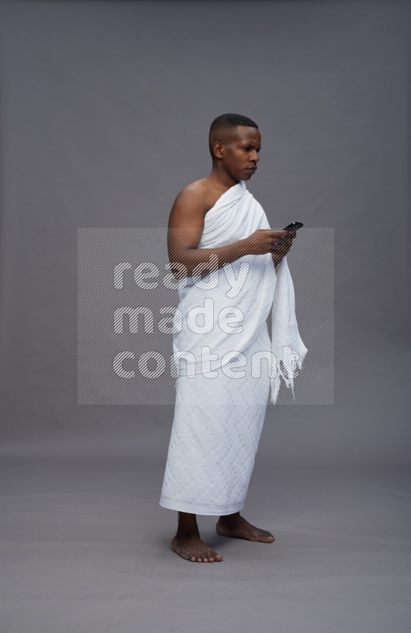 A man wearing Ehram Standing texting on phone on gray background