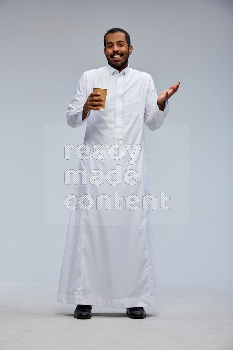 Saudi man wearing thob standing holding paper cup on gray background