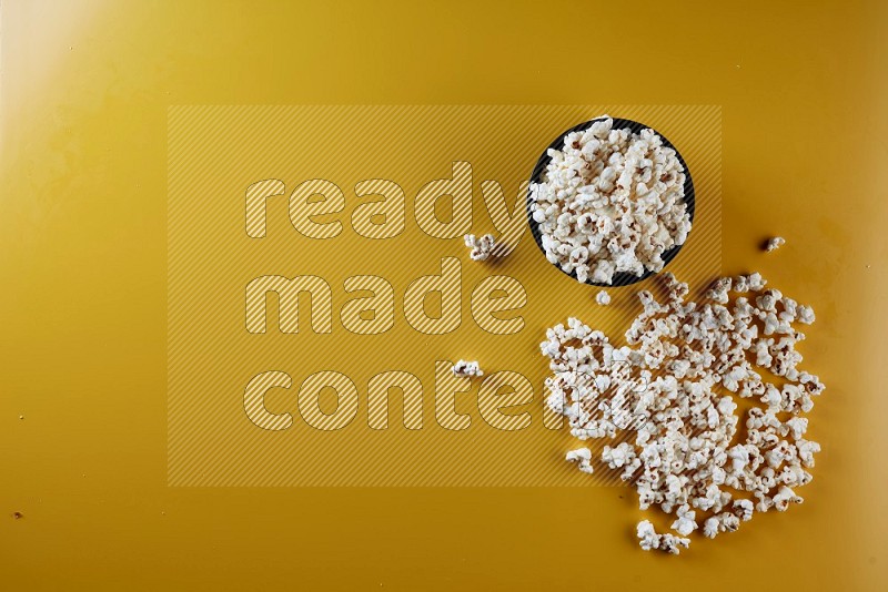 A black ceramic bowl full of popcorn with popcorn beside it on a yellow background in different angles
