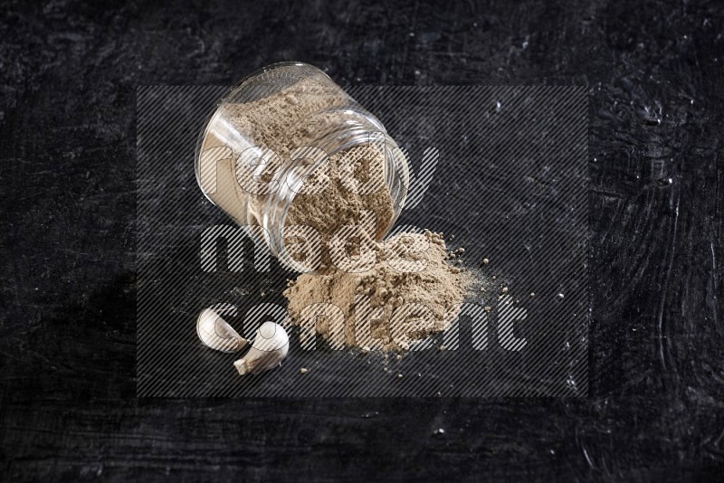 A glass jar full of garlic powder flipped and the powder came out on a textured black flooring in different angles