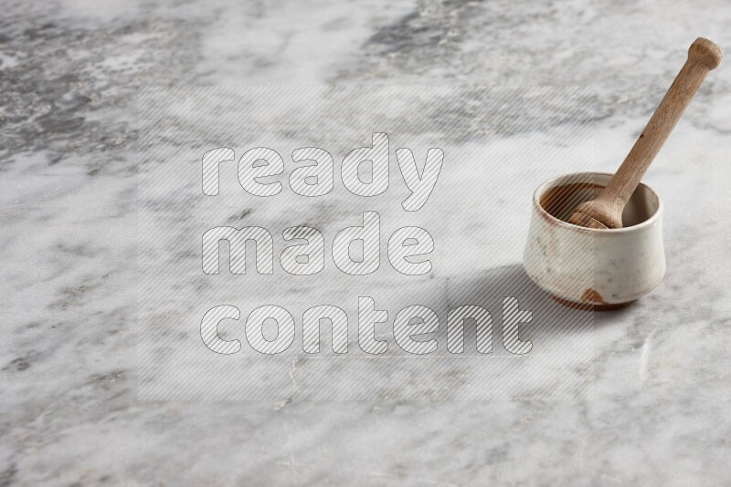 Beige pottery bowl with wooden honey dipper in it on grey marble background
