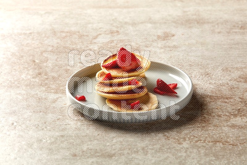 Five stacked strawberry mini pancakes in a blue plate on beige background