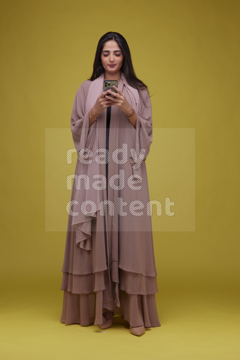 A woman Texting on a Yellow Background wearing Brown Abaya