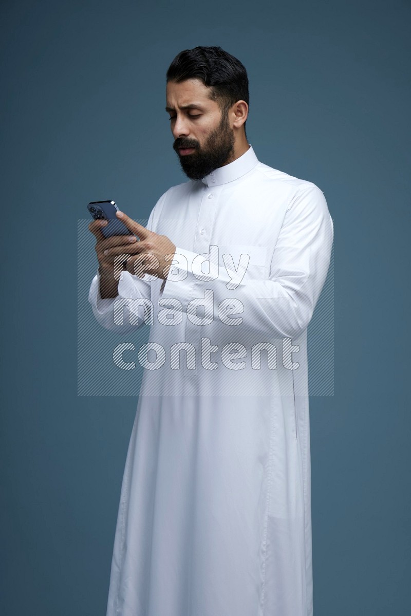 A man Texting in a blue background wearing Saudi Thob