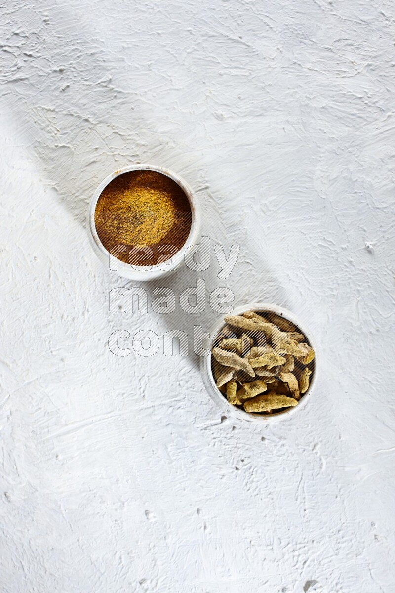 2 beige pottery bowl full of turmeric powder and dried turmeric whole fingers on textured white flooring