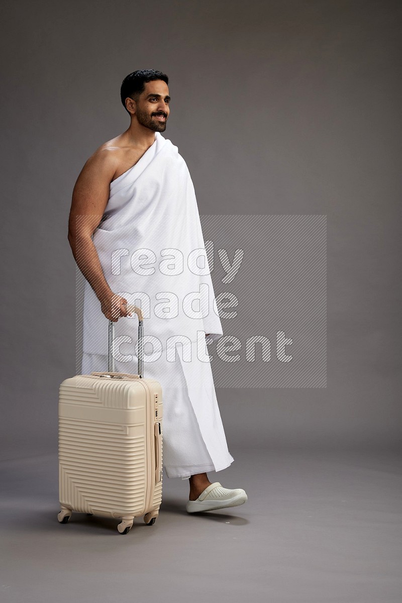 A man wearing Ehram Standing holding traveling bag on gray background