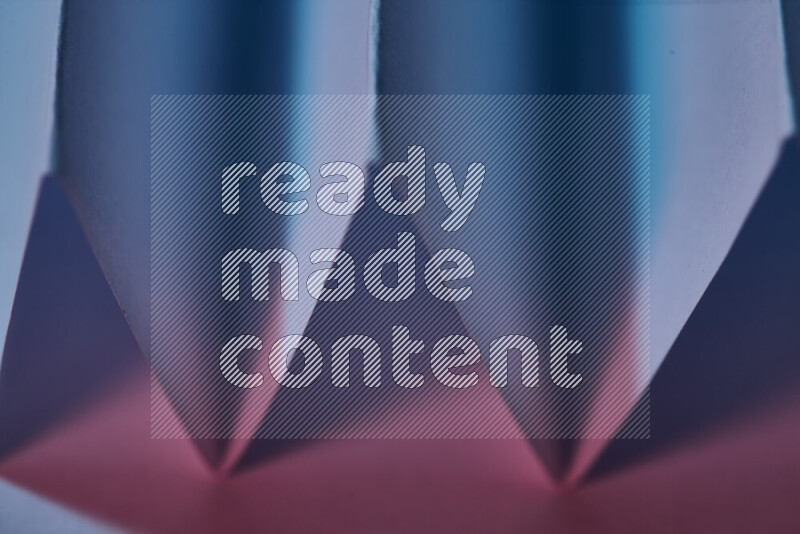 A close-up abstract image showing sharp geometric paper folds in blue and pink gradients