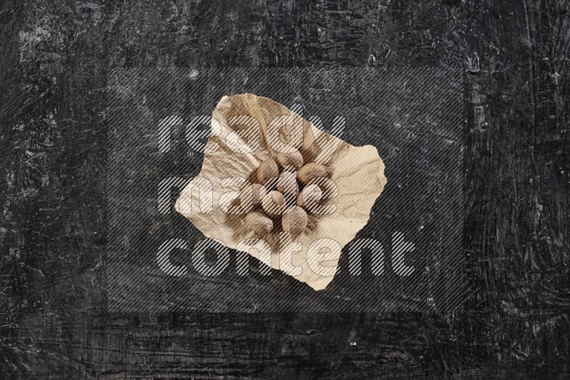 A crumpled piece of paper full of nutmeg on a textured black flooring in different angles