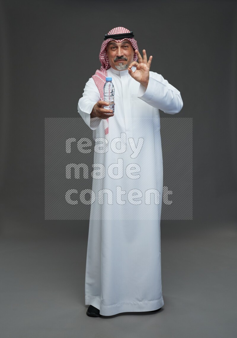 Saudi man with shomag Standing drinking water on gray background