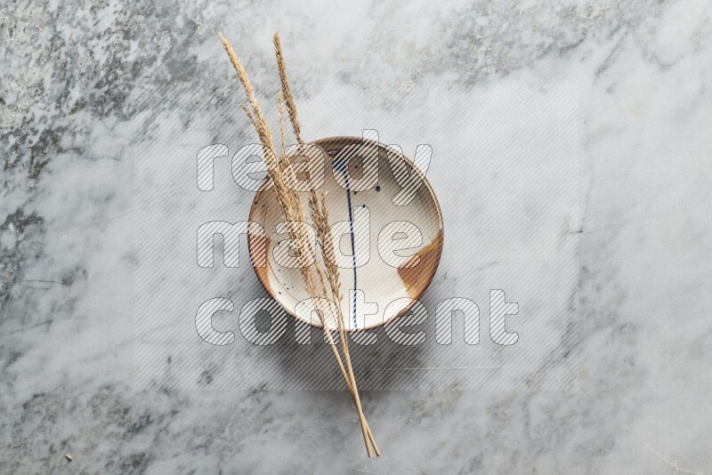 Wheat stalks on multicolored pottery plate on grey marble background