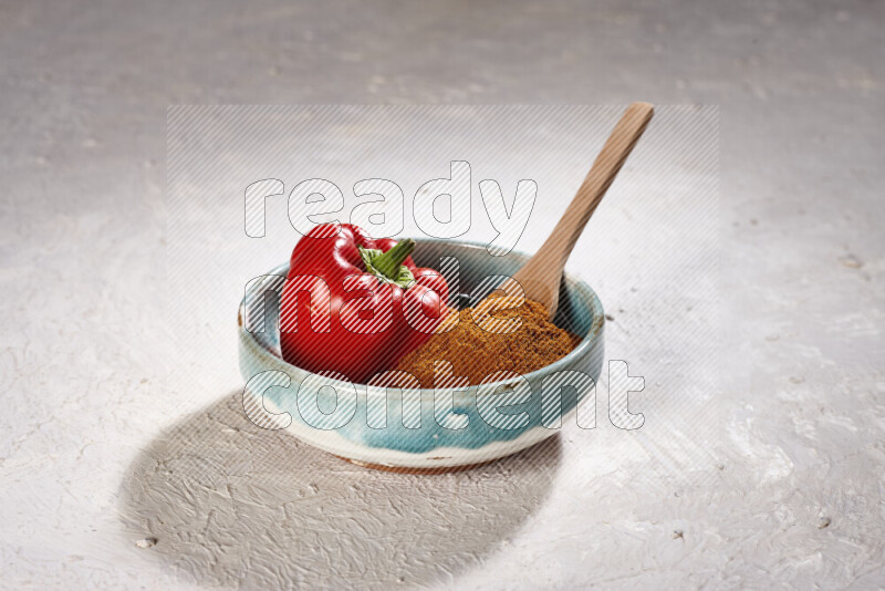 A colored pottery plate full of ground paprika powder and red bell pepper on white background