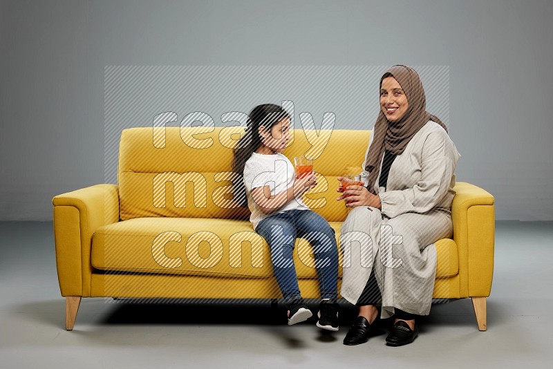 Mom and daughter sitting drinking juice on gray background