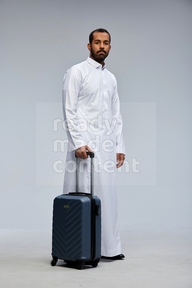 Saudi man wearing thob standing holding Travel bag on Gray background