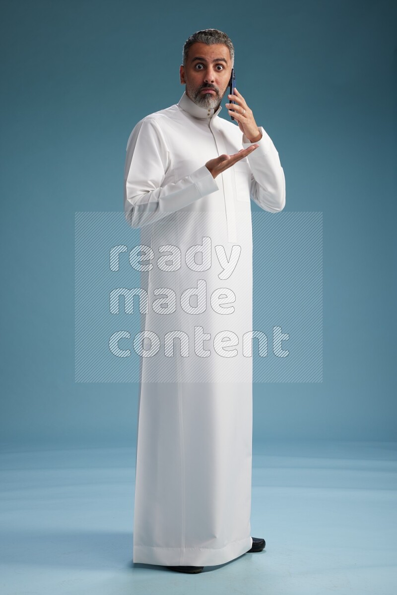 Saudi man wearing thob talking on the phone on blue background