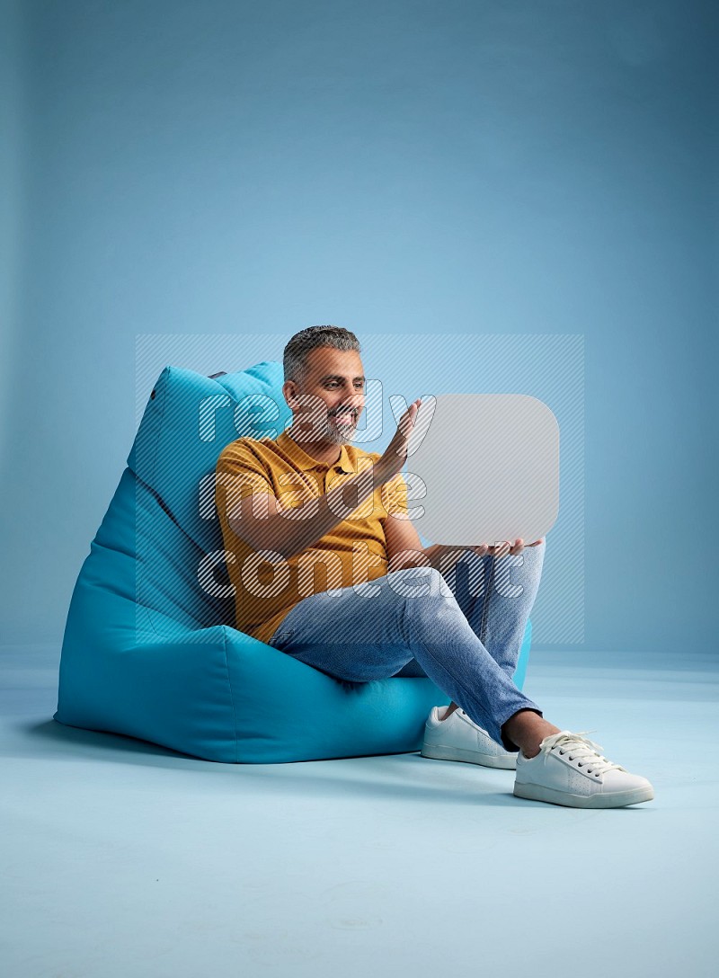 A man sitting on a blue beanbag and holding social media sign