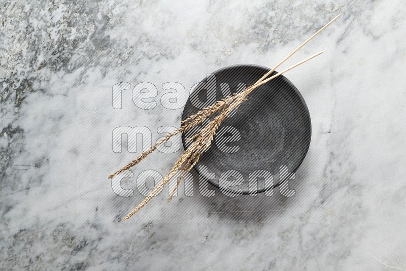 Wheat stalks on Black Pottery Plate on grey marble flooring, Top view