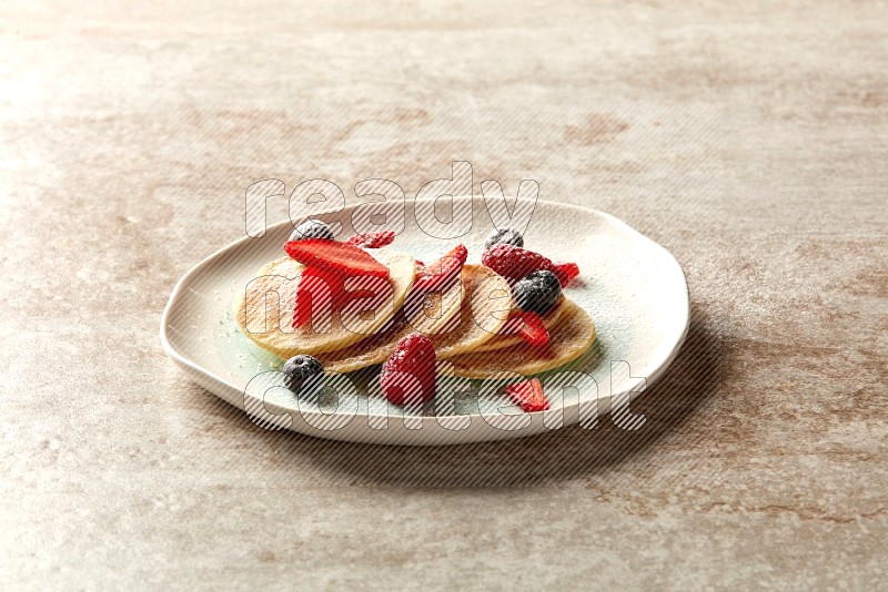 Five stacked mixed berries mini pancakes in a bicolor plate on beige background