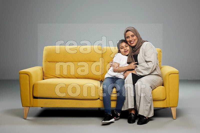 A girl with her mother sitting and interacting with the camera on gray background