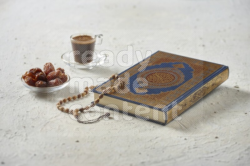 Quran with dates, prayer beads and different drinks all placed on textured white background