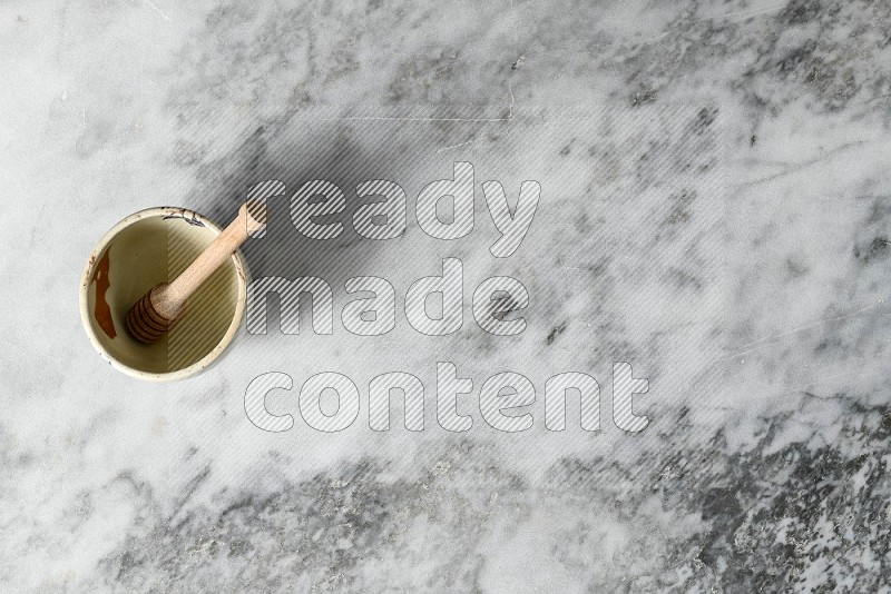 Decorative Pottery Bowl with wooden honey handle in it, on grey marble flooring, Top View