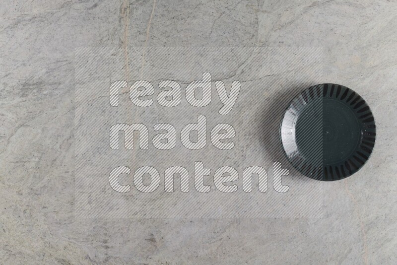 A dark green pottery plate on grey marble background
