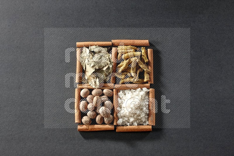 4 squares of cinnamon sticks full of bay laurel leaves, white salt, turmeric fingers and nutmegs on black flooring