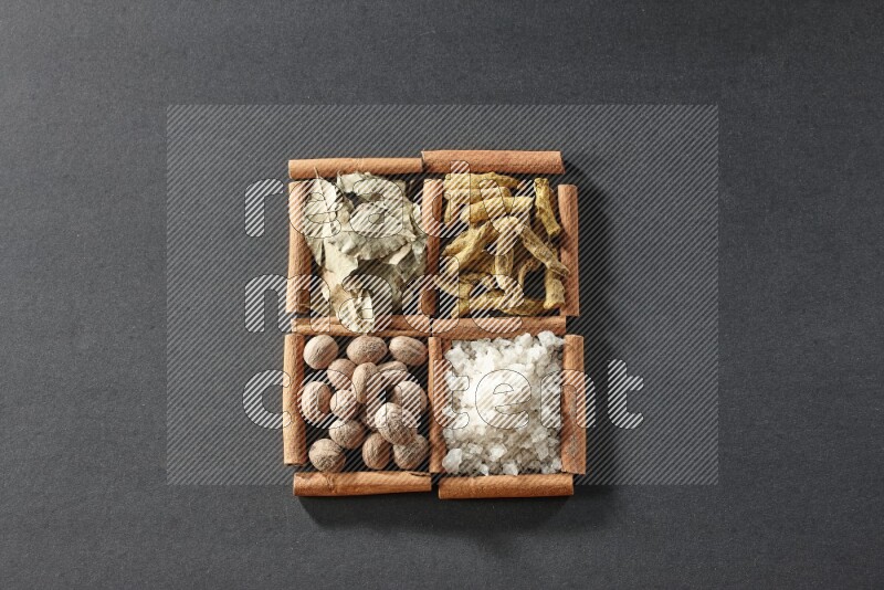 4 squares of cinnamon sticks full of bay laurel leaves, white salt, turmeric fingers and nutmegs on black flooring