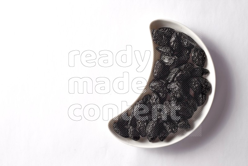 Dried plums in a crescent pottery plate on white background